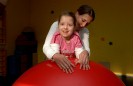 Eine Physiotherapeutin behandelt ein Kind auf dem Therapieball.